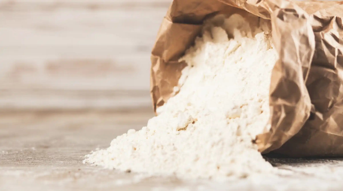 Farine italienne type 00 versée d’un sac en papier sur un plan de travail, idéale pour pizzas et pâtes fraîches.