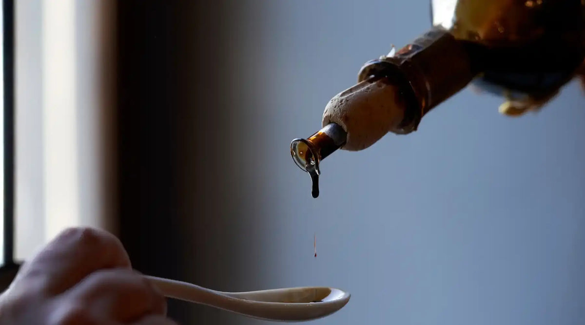 Goutte de vinaigre balsamique tombant d’une bouteille dans une cuillère, symbole de tradition et raffinement italien.