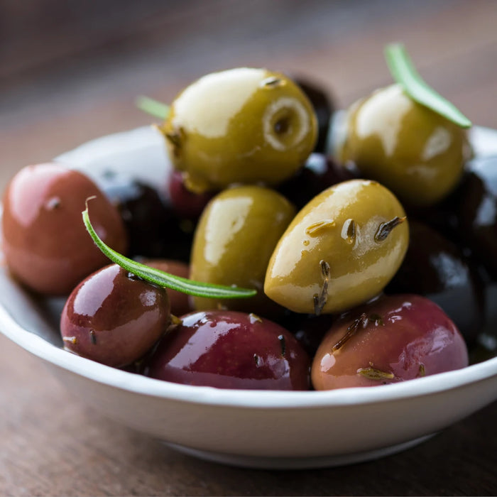 Bol d'olives marinées vertes et noires, assaisonnées avec du romarin et des herbes aromatiques, présenté sur une table en bois.