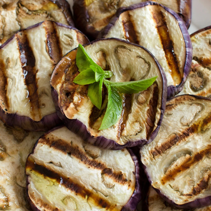 Tranches d'aubergines grillées avec des marques de cuisson, disposées sur une assiette blanche et garnies d'une feuille de basilic frais.