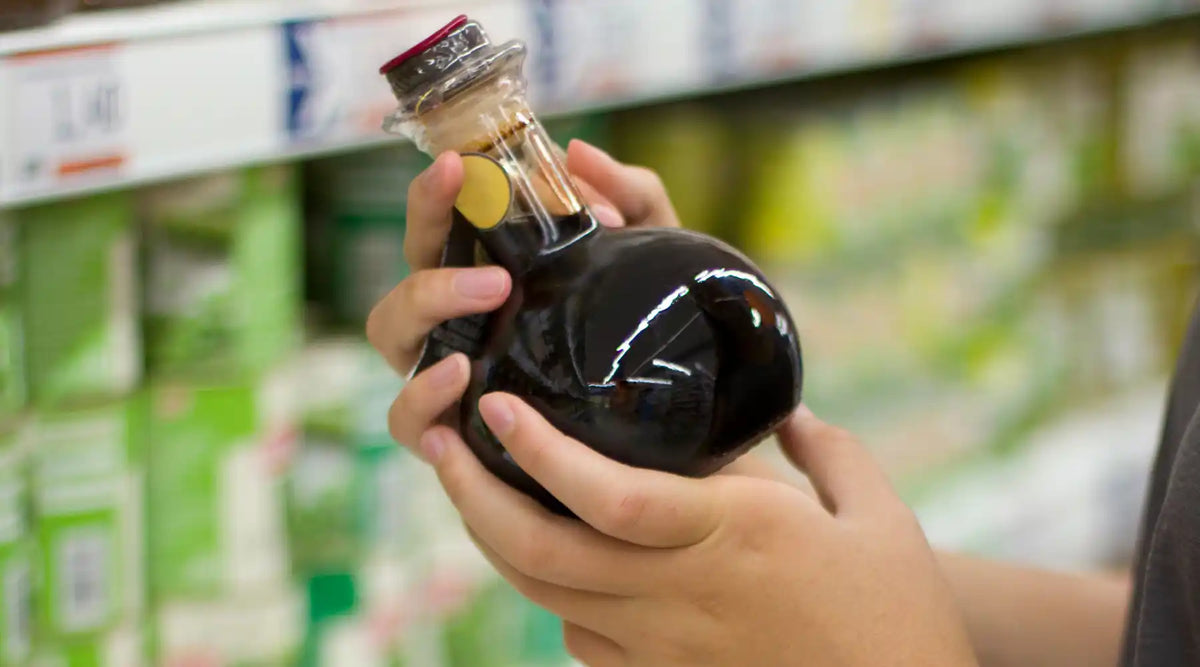 Personne tenant une bouteille de crème balsamique dans un rayon de supermarché