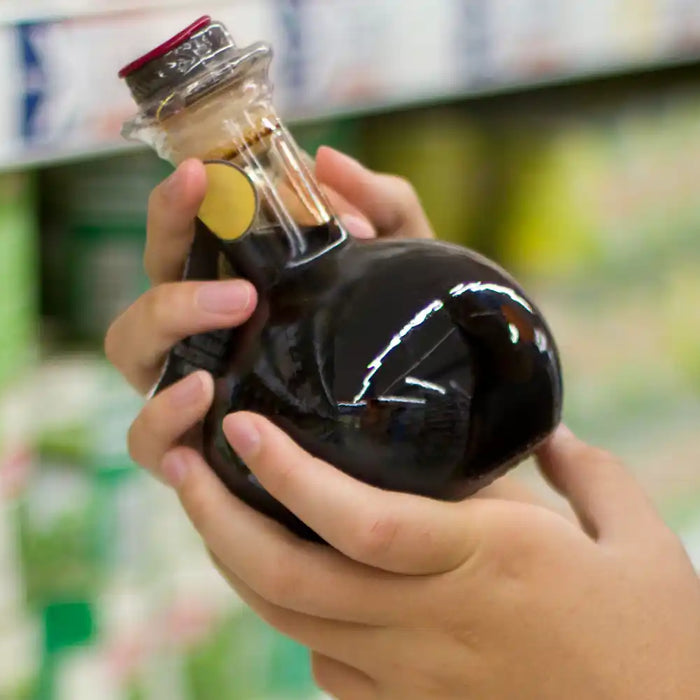 Personne tenant une bouteille de crème balsamique dans un rayon de supermarché