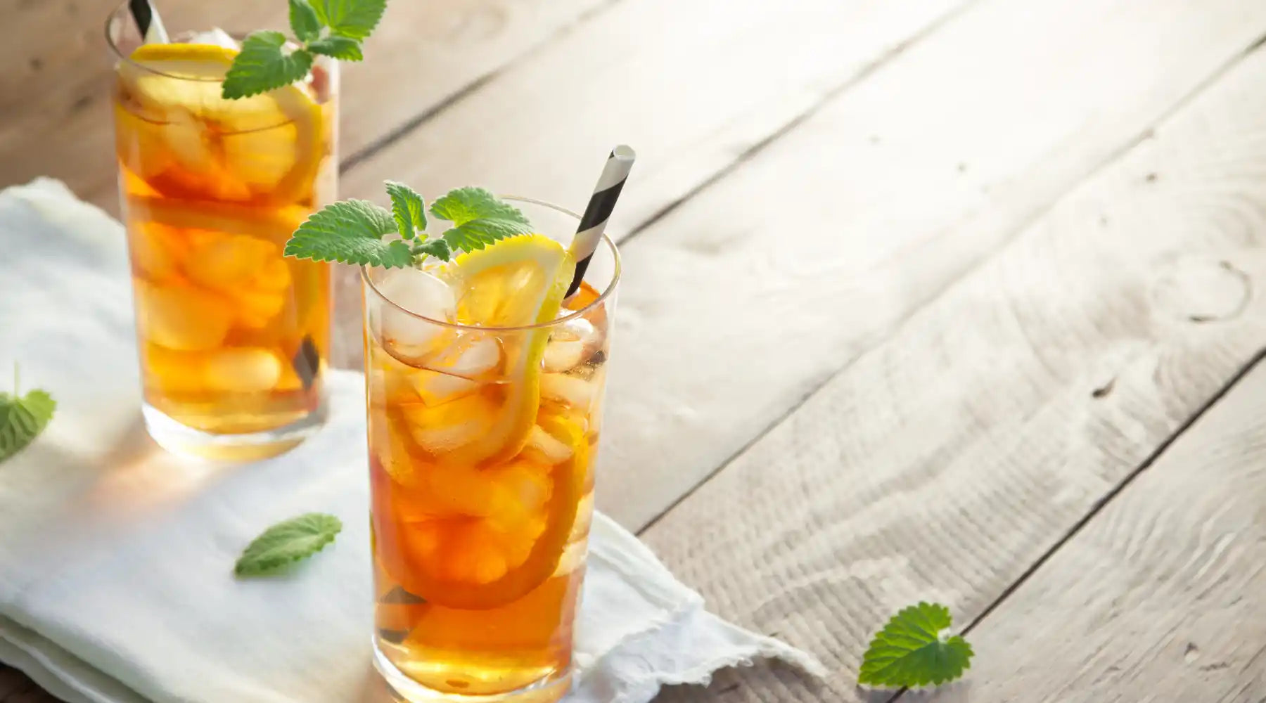 Deux verres de thé glacé au citron avec glaçons et feuilles de menthe sur une table estivale.