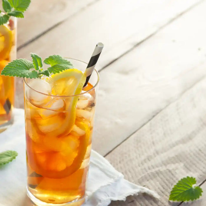 Deux verres de thé glacé au citron avec glaçons et feuilles de menthe sur une table estivale.