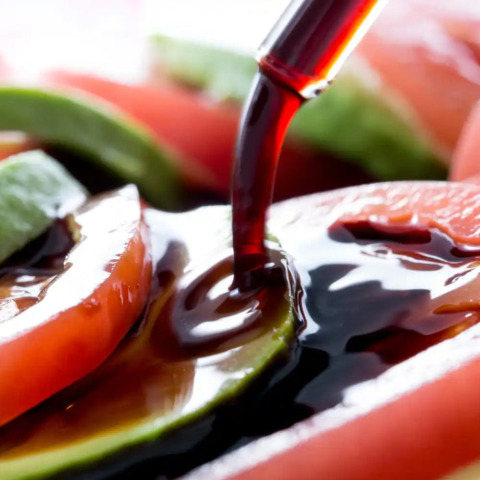 Tranches de tomates et d’avocats nappées de vinaigre balsamique versé délicatement.